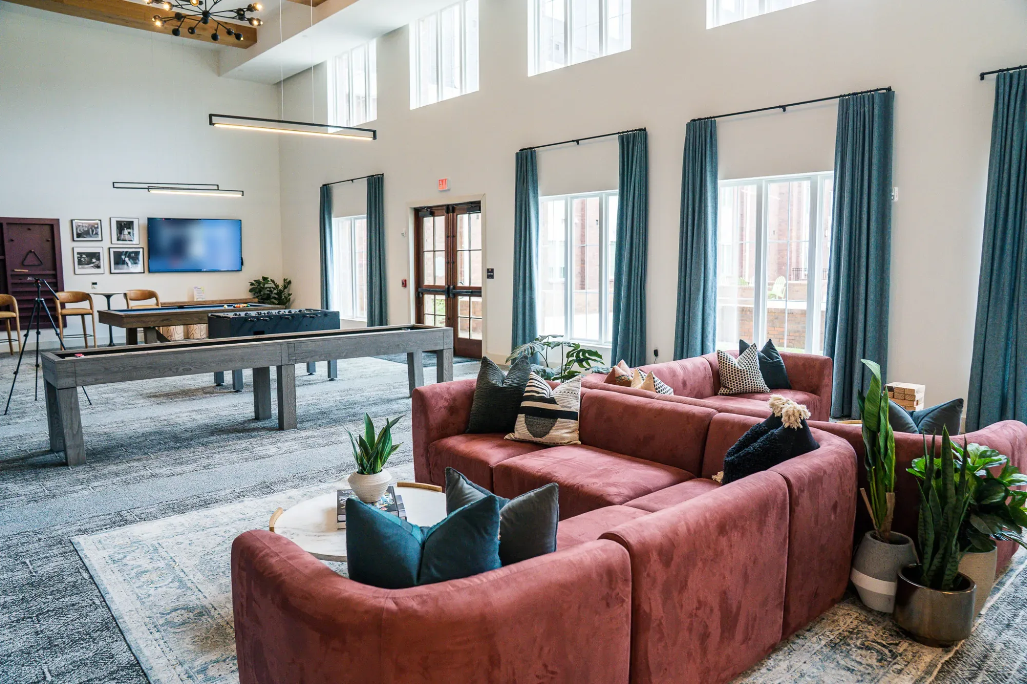 Clubhouse lounge at an apartment community with a sofa, game tables and tall windows